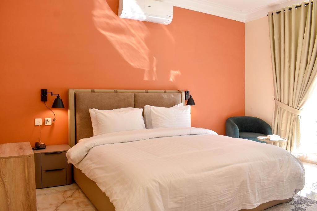 Una habitación de hotel con cama, mesitas de noche, lámpara, una silla y ventana con cortinas.