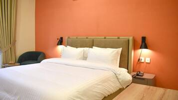 A hotel room with a bed, bedside tables, a chair, and an air conditioning unit.