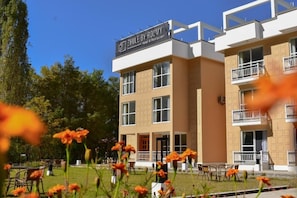 A hotel with a sign reading 'ZHULE BY ROOMY Hotel & Restaurant' with a two-story building, balconies, and a garden area with flowers.