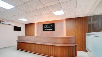 A reception desk with a wooden finish, a sign above it, and a tiled ceiling with recessed lighting.