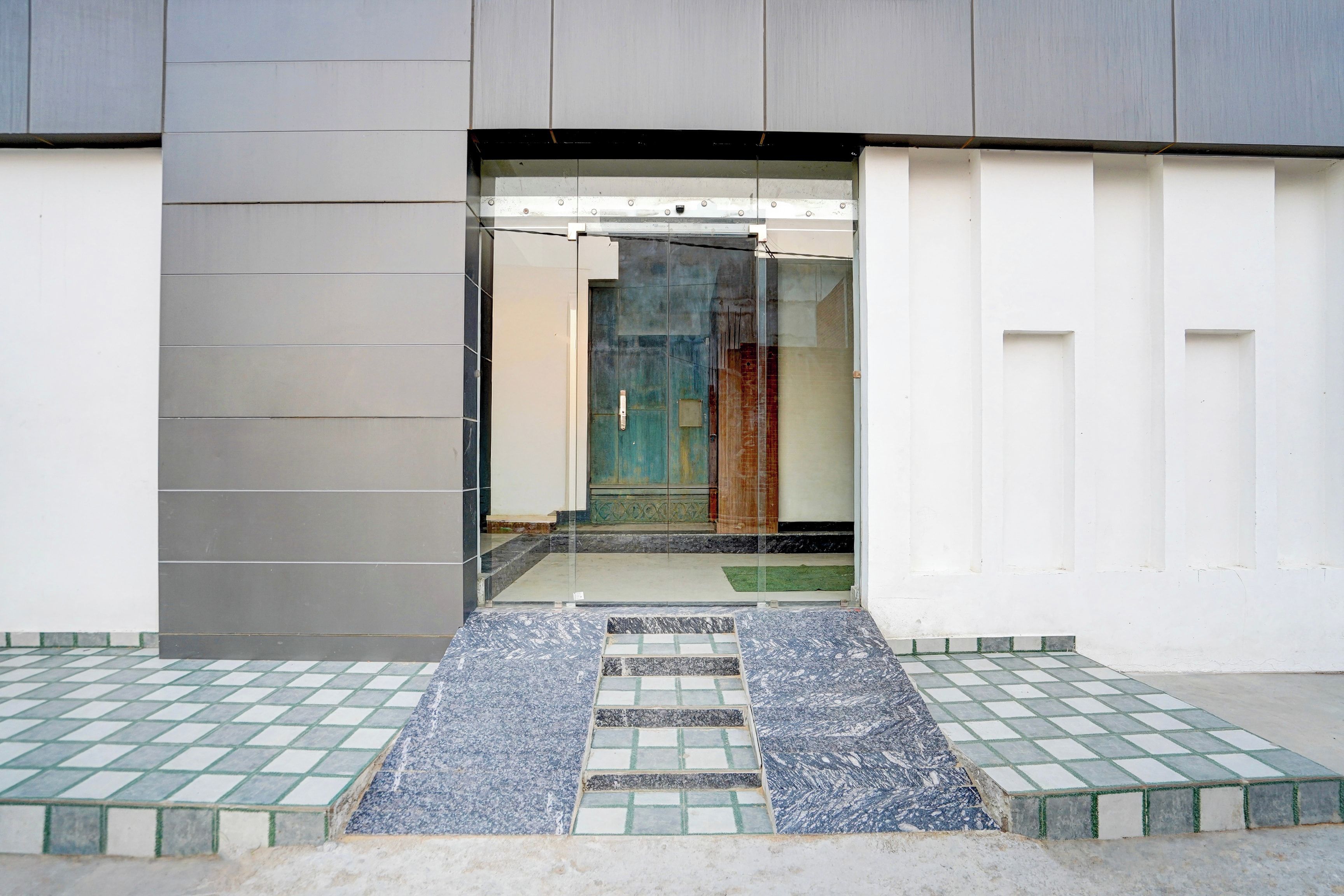 Una entrada moderna con puerta de vidrio, un sendero con losetas que conduce a una puerta y una reja de metal.