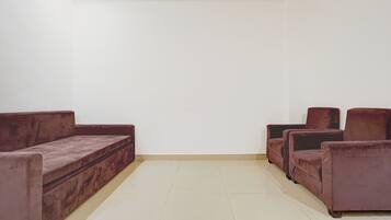 Una habitación con piso de baldosas color beige, techo blanco y un juego de sofá marrón.