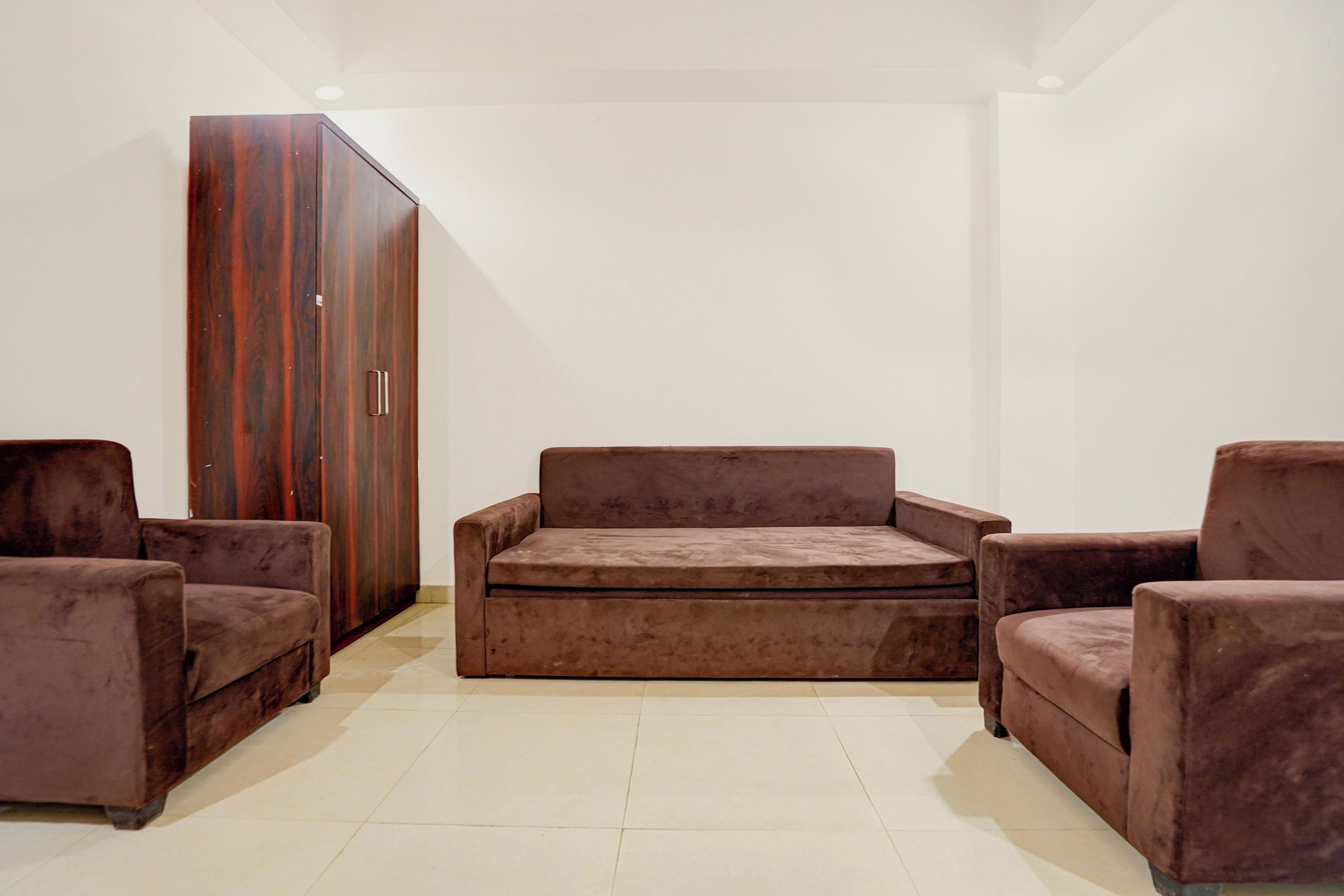 Une pièce avec un canapé marron, deux fauteuils et une armoire en bois.