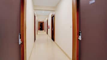 Un corridoio d'albergo con porte provviste di numeri civici, un estintore e un lampadario a soffitto.