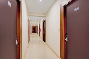 Pasillo de hotel con puertas numeradas, un extintor y un accesorio de iluminación en el techo.