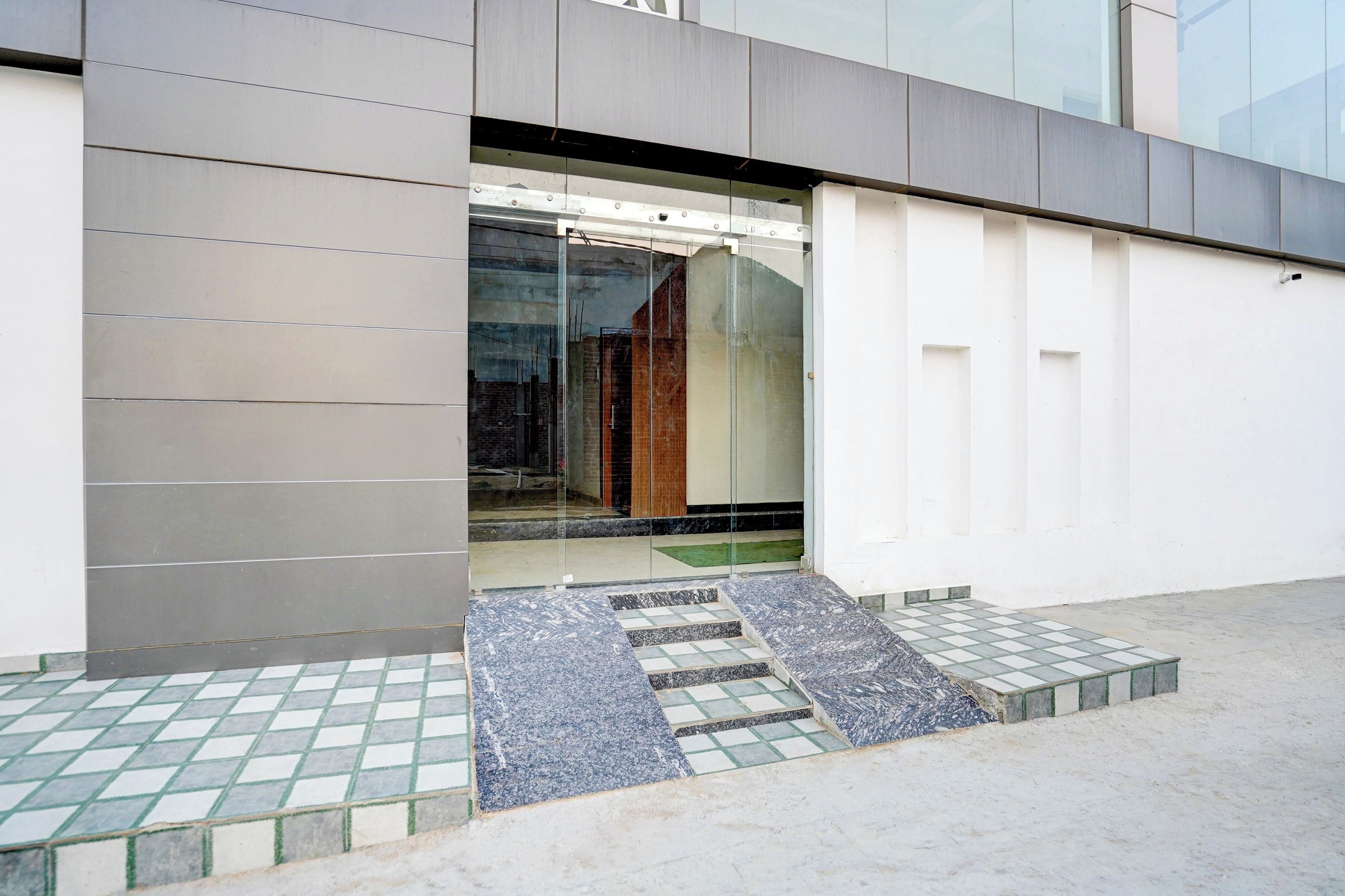 A modern building entrance with a glass door, a metal staircase, and a tiled ground floor.