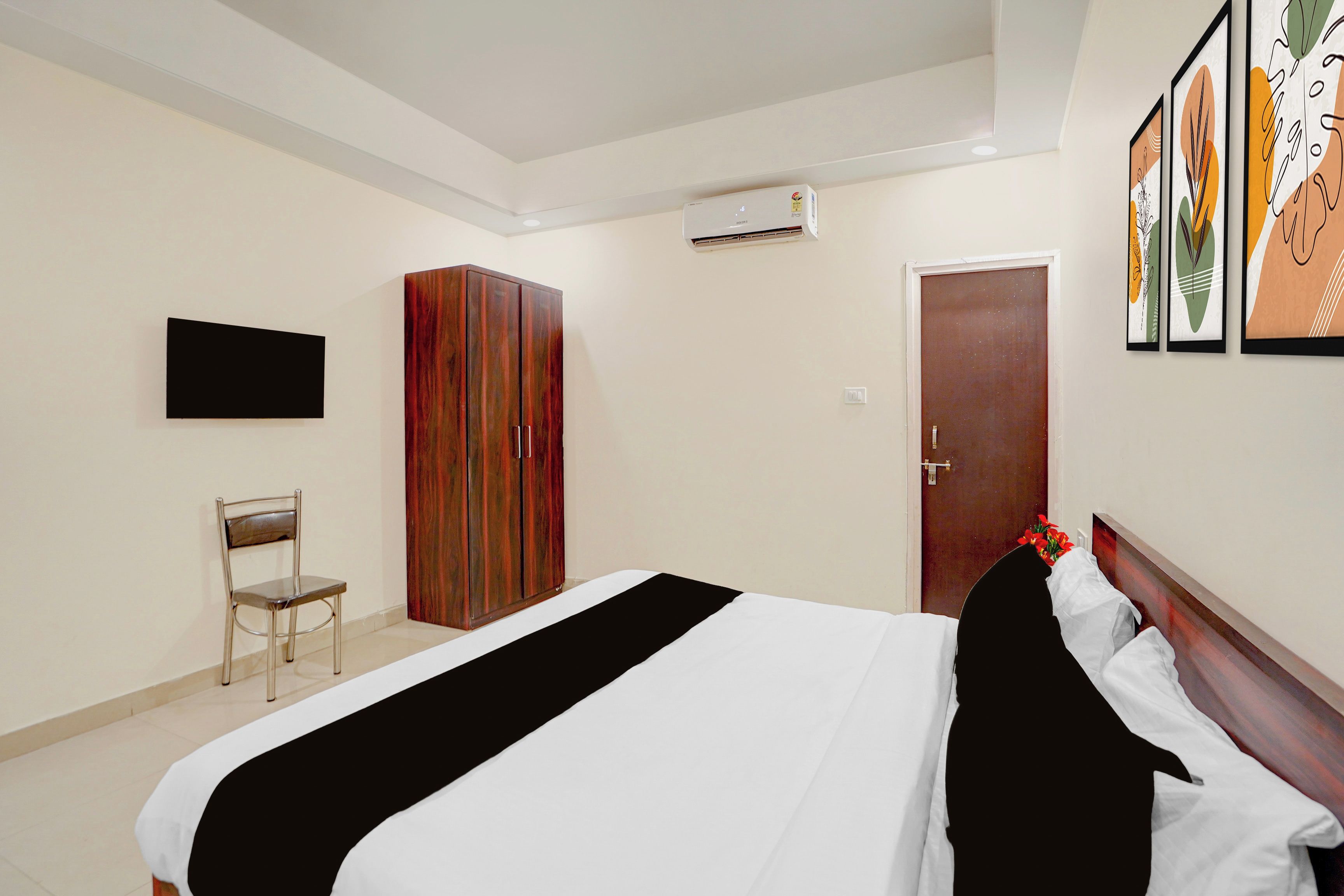 A hotel room with a bed, a wardrobe, a chair, an air conditioning unit, and a door.
