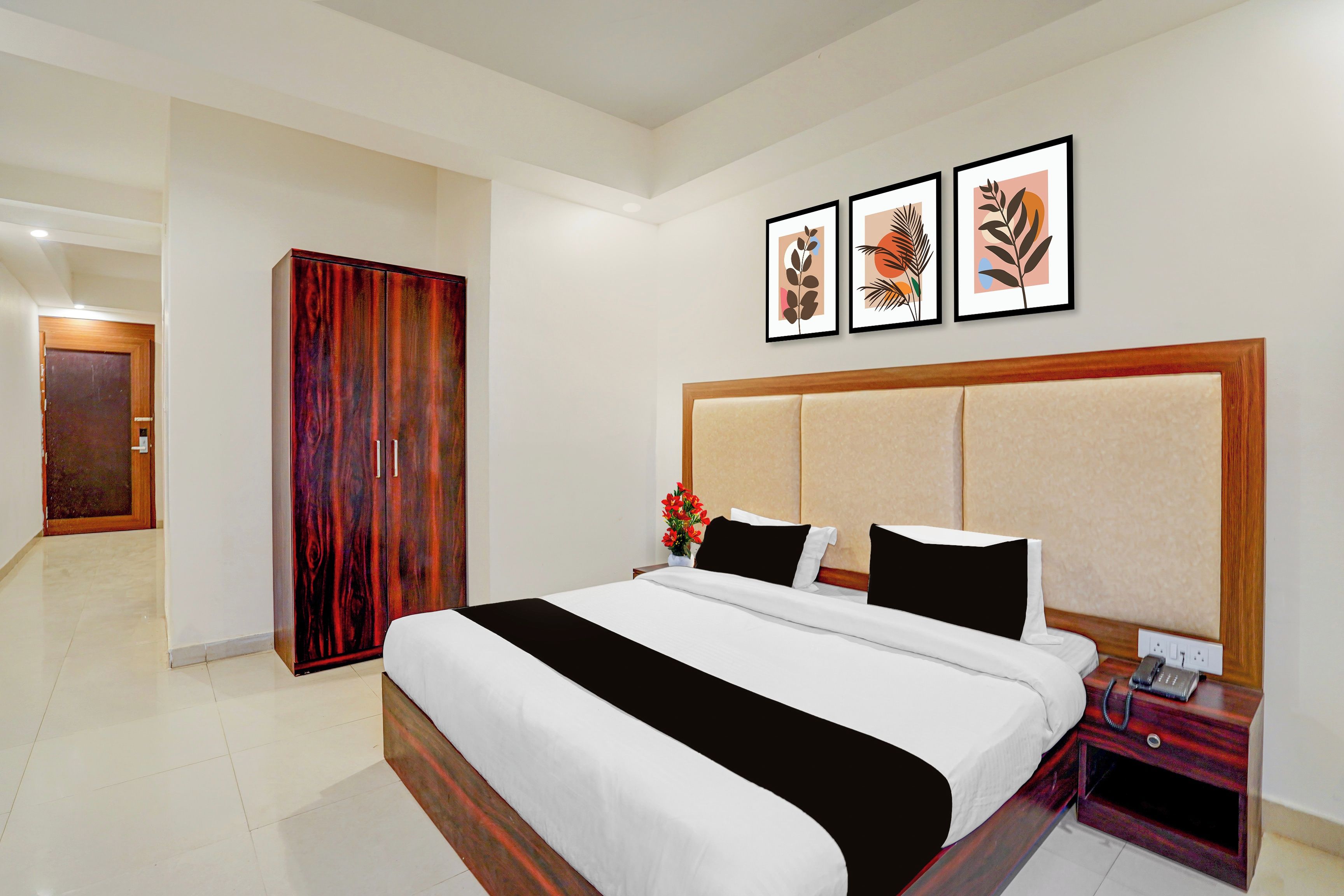 A hotel room with a large bed, a wardrobe, a bedside table with a phone, and three framed artworks on the wall.