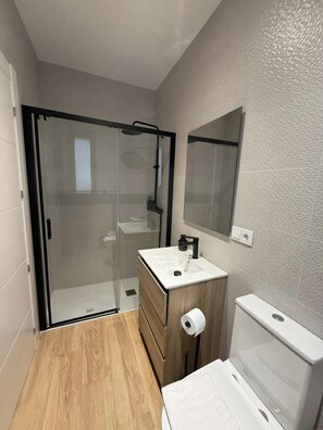 A modern bathroom with a glass shower enclosure, a wooden vanity with a sink, and a toilet. - Aires de Salamanca Melibea (Salamanca)