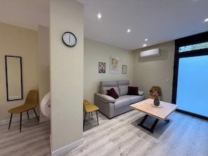 A modern living room with a sofa, a coffee table, and a dining table. There is a clock on the wall and artwork above the sofa. - Aires de Salamanca Melibea (Salamanca)