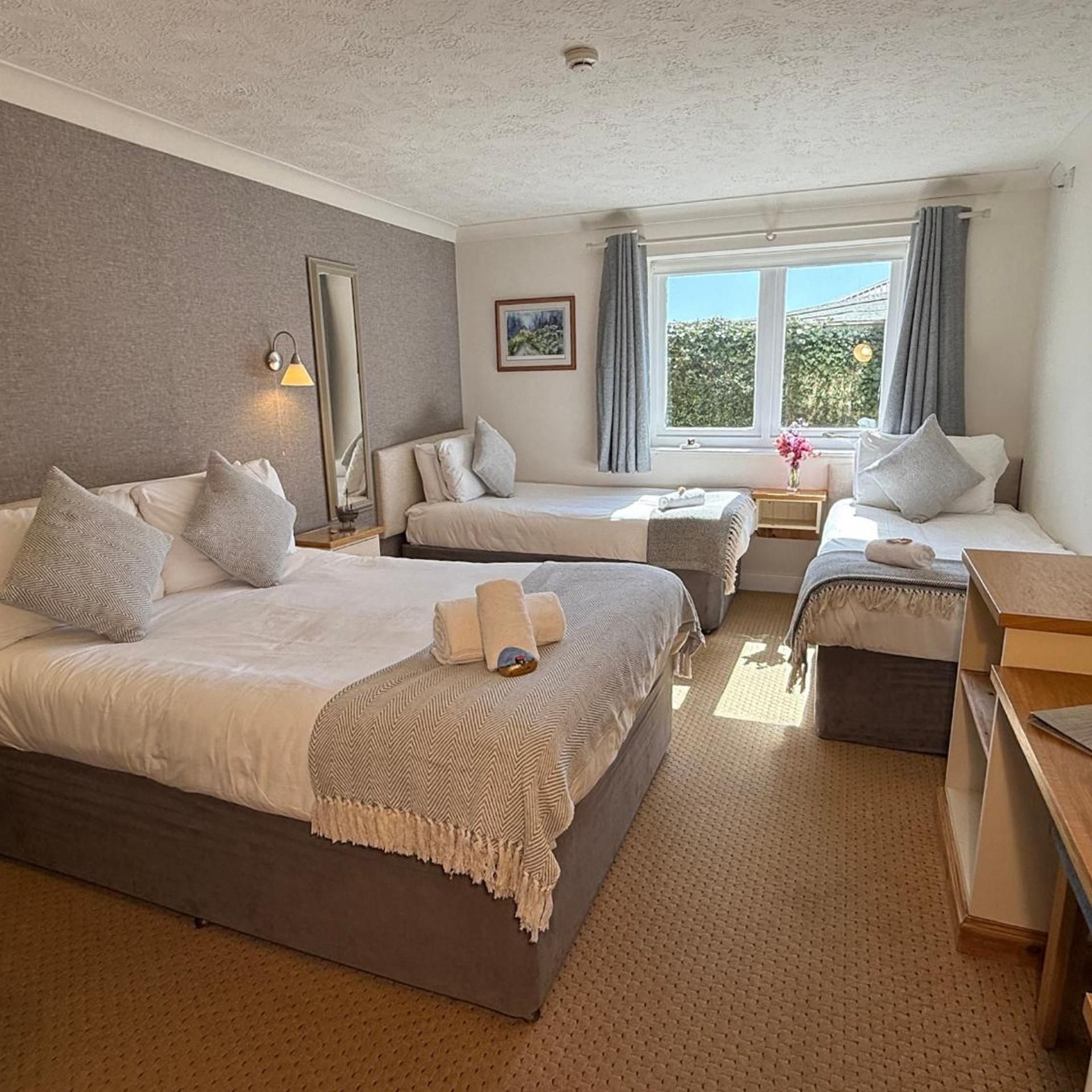 A hotel room with two beds, a sitting area, a window with curtains, and a painting on the wall.