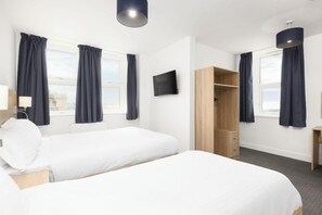 A hotel room with two beds, a TV, a wardrobe, and a window with curtains. - The Sandringham Hotel (Weston-super-Mare)