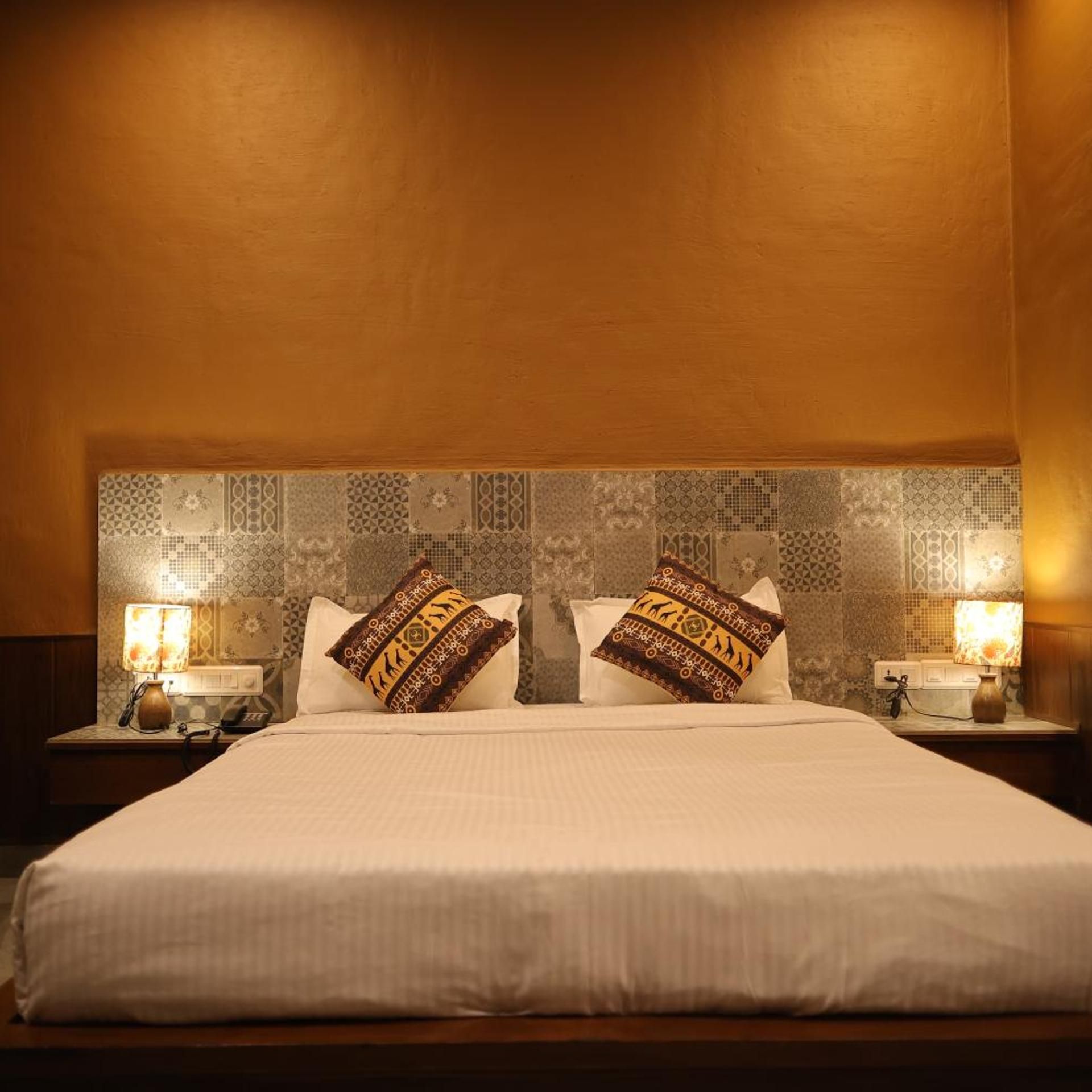 A hotel room with a large bed, two bedside lamps, and patterned wall tiles.