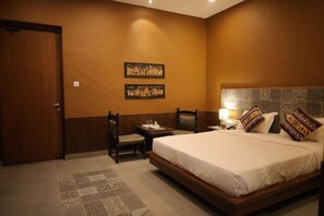 Ein Hotelzimmer mit einem großen Bett, einem Holzstuhl, einem kleinen Tisch und zwei an der Wand befestigten Bildern.