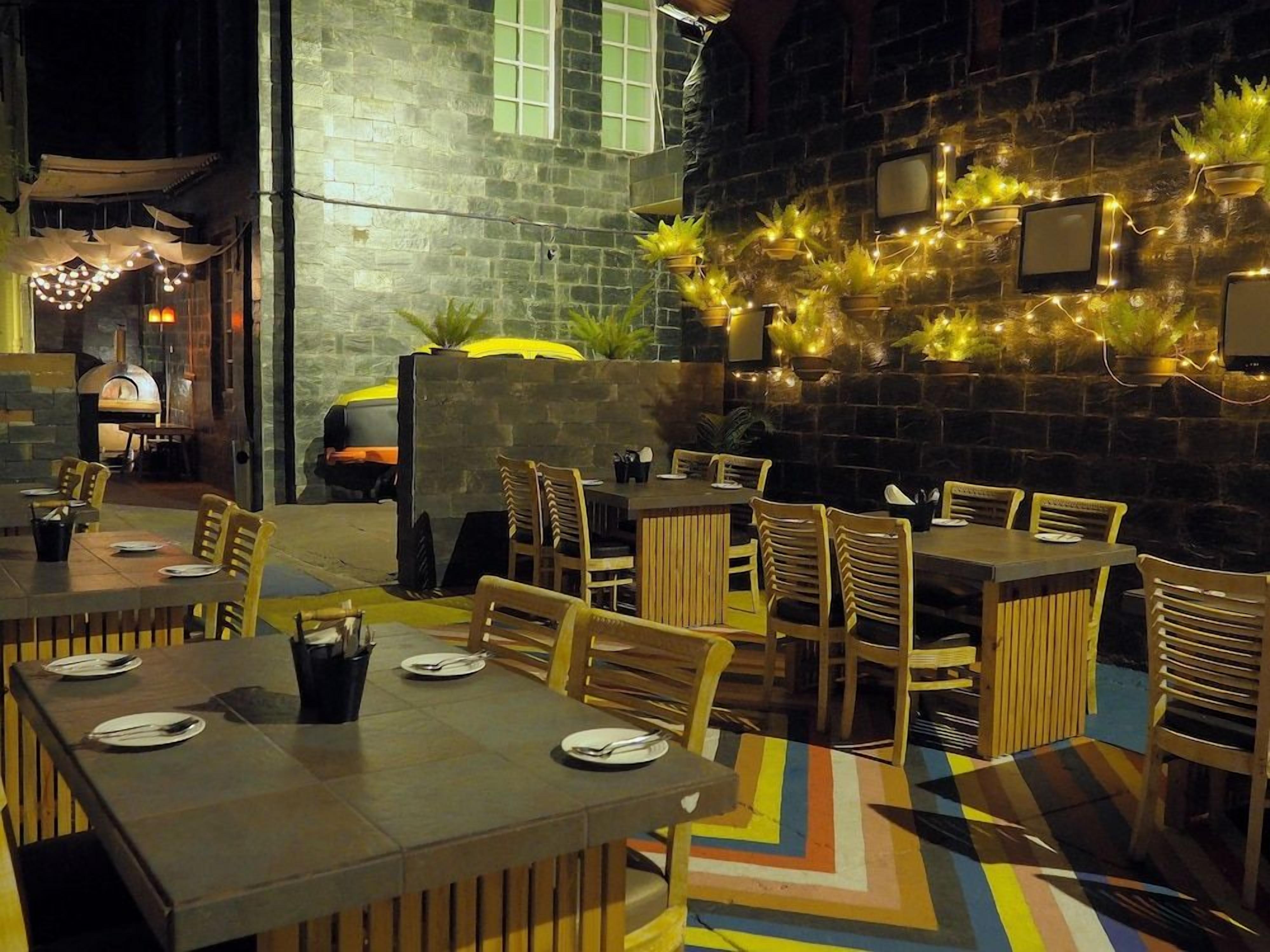 An outdoor dining area with tables and chairs, a brick wall, and string lights.