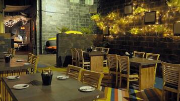 An outdoor dining area with tables and chairs, a brick wall, and string lights.
