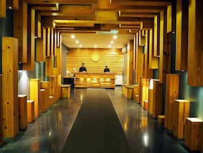 Un área de recepción con un mostrador de madera, dos empleados y una pared con diseño en el fondo.
