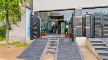 Entrada moderna de un edificio con puerta de vidrio, un conjunto de escaleras que conducen a la entrada y un árbol a la izquierda.