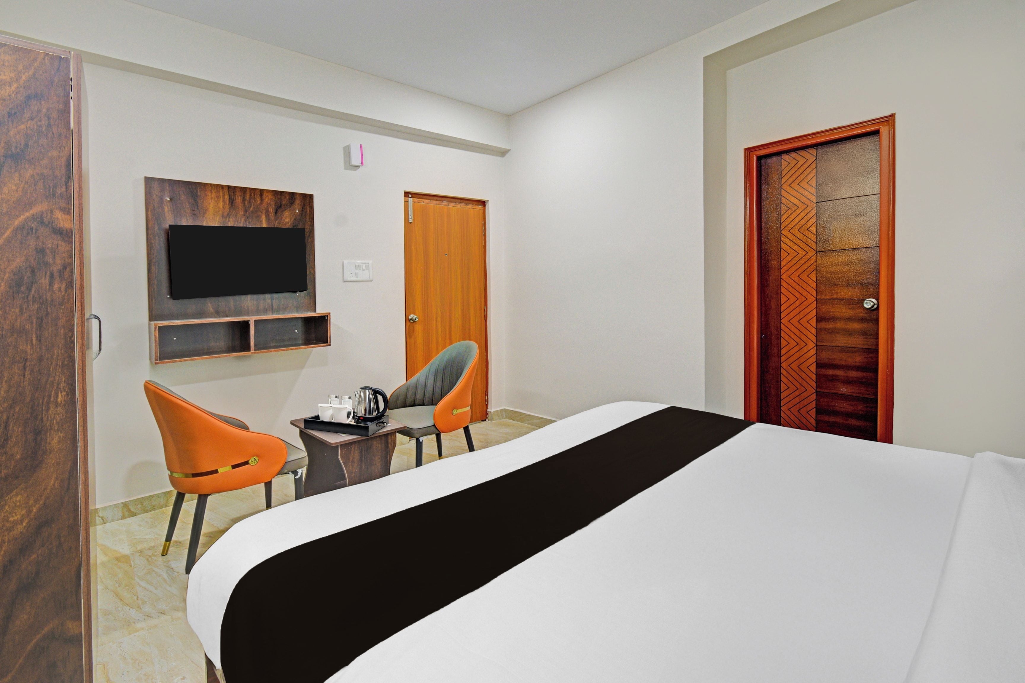 A hotel room with a bed, two chairs, a small table, a television, and a door with a decorative panel.