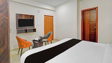 Habitación de hotel con una cama, dos sillas, una mesita, un televisor y una puerta con un panel decorativo.