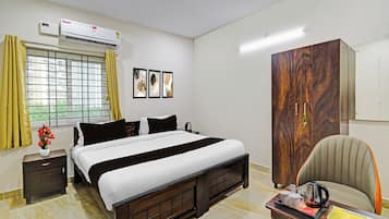 Habitación de hotel con cama, escritorio con hervidor, silla, armario, ventana con cortinas y decoración en la pared.