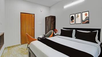 A hotel room with a bed, a wooden wardrobe, a desk with a chair, and artwork on the wall.