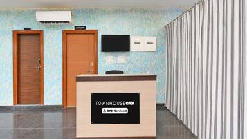 A reception desk with a sign indicating 'TOWNHOUSE OAK' and 'OYO-Serviced' amenities. There are two doors, a mounted television, and a patterned wall.