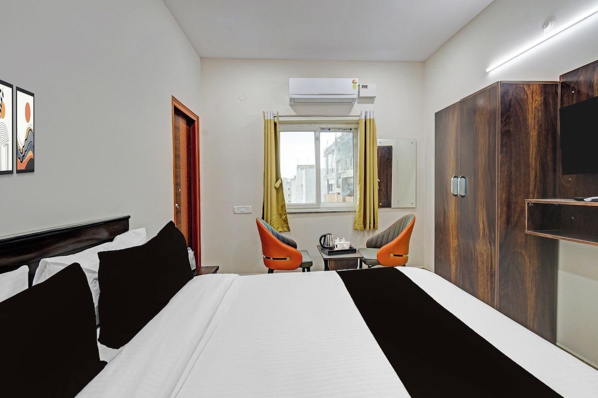 Ein Hotelzimmer mit Bett, zwei Stühlen, einem kleinen Tisch mit Tablett und einem Fenster mit Vorhängen.