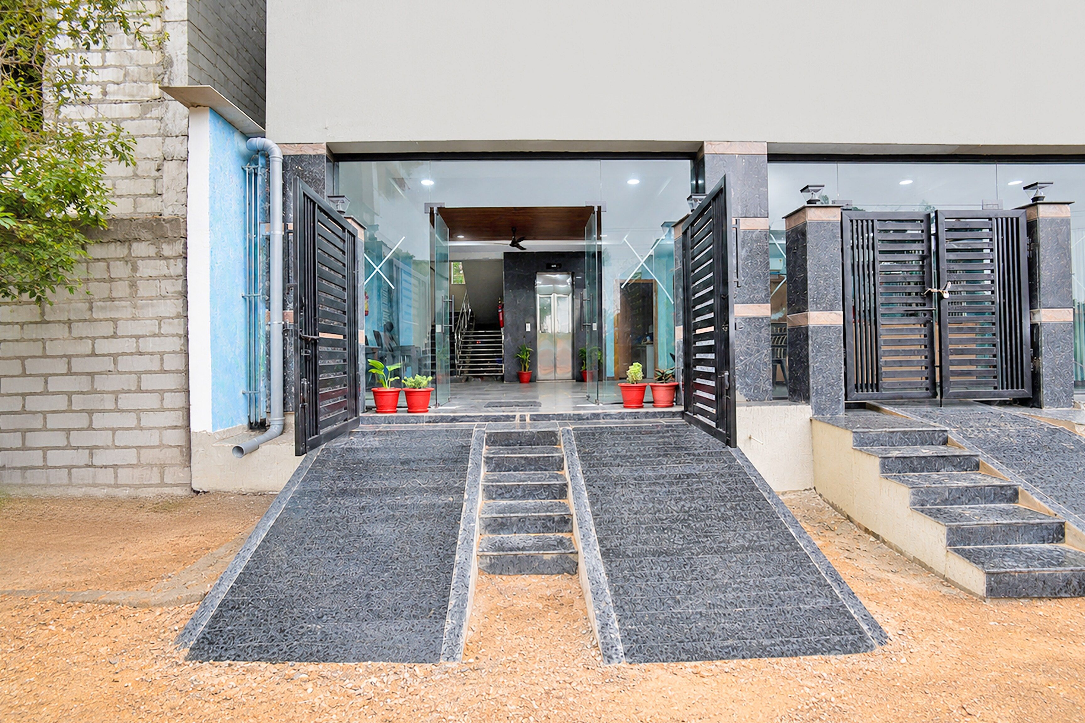 A building entrance with a set of stairs leading up to a door, flanked by two large black gates.