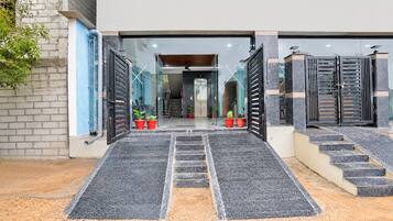 A building entrance with a set of stairs leading up to a door, flanked by two large black gates.