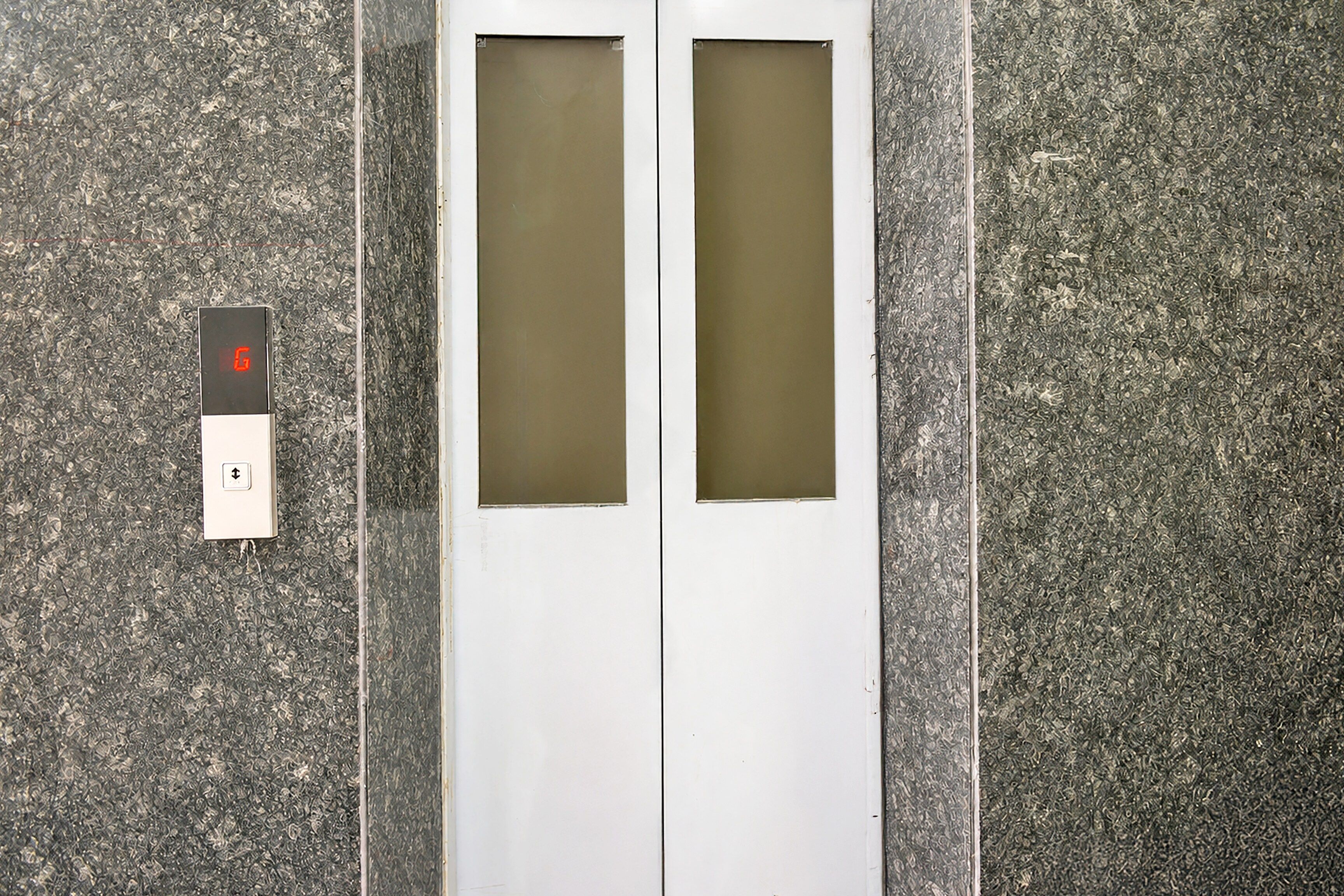 Un ascensor con dos paneles de vidrio y un panel de control con un indicador luminoso rojo.