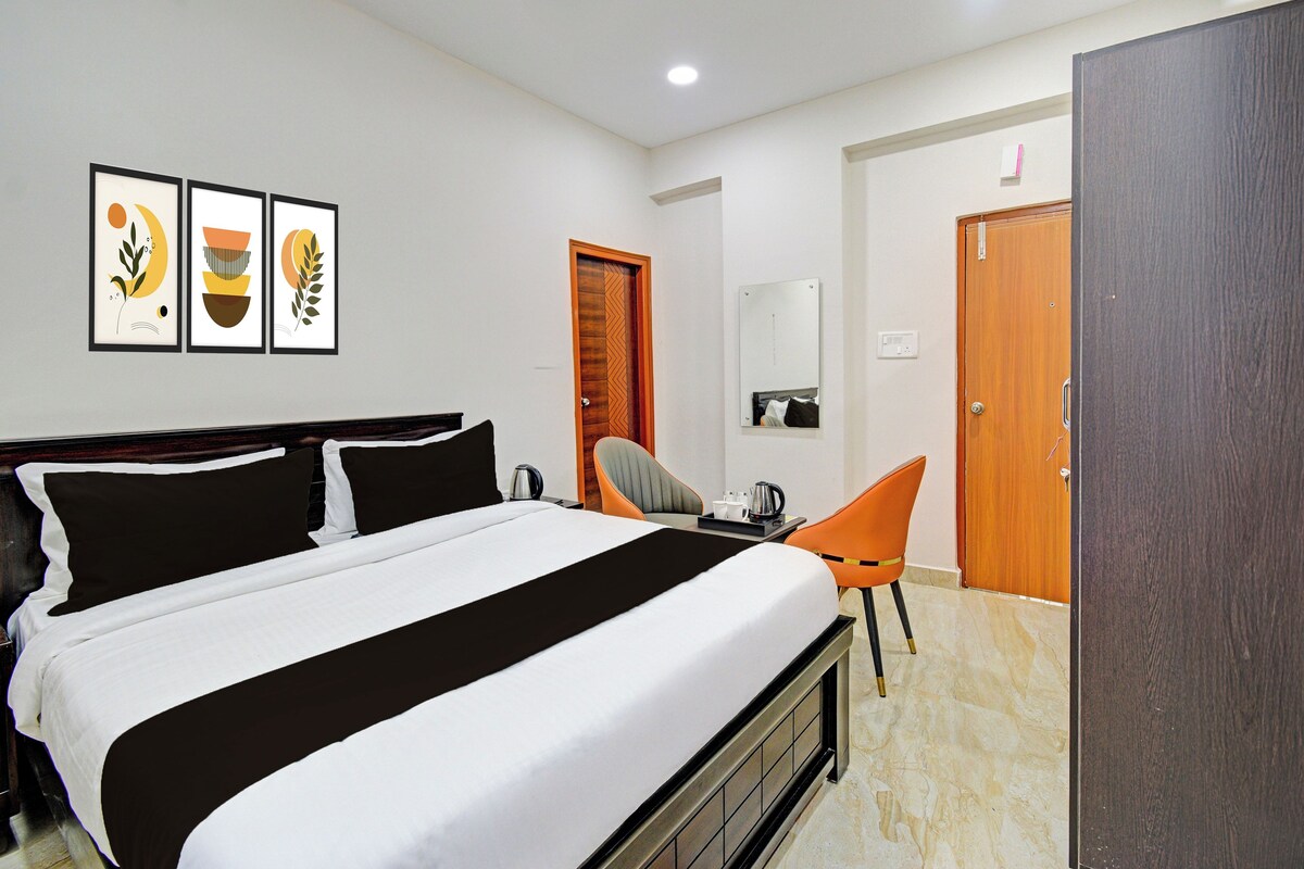 A hotel room with a bed, a desk, a chair, and a wardrobe. There are framed pictures on the wall.