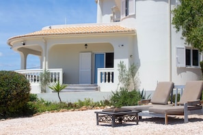 A white building with a tiled roof, a covered porch, and a gravel patio with outdoor furniture. - Casa Piscaretta with heated pool and close to sandy beaches (Porches)