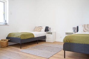 Et moderne soveværelse med to senge, et natbord, en kurv og et vindue med en plante.