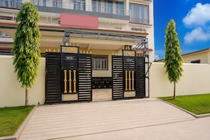 A gated entrance to a residential building with a paved driveway and two tall trees on either side. - Collection O IIT BHU Susu Wahi Varanasi (Varanasi)