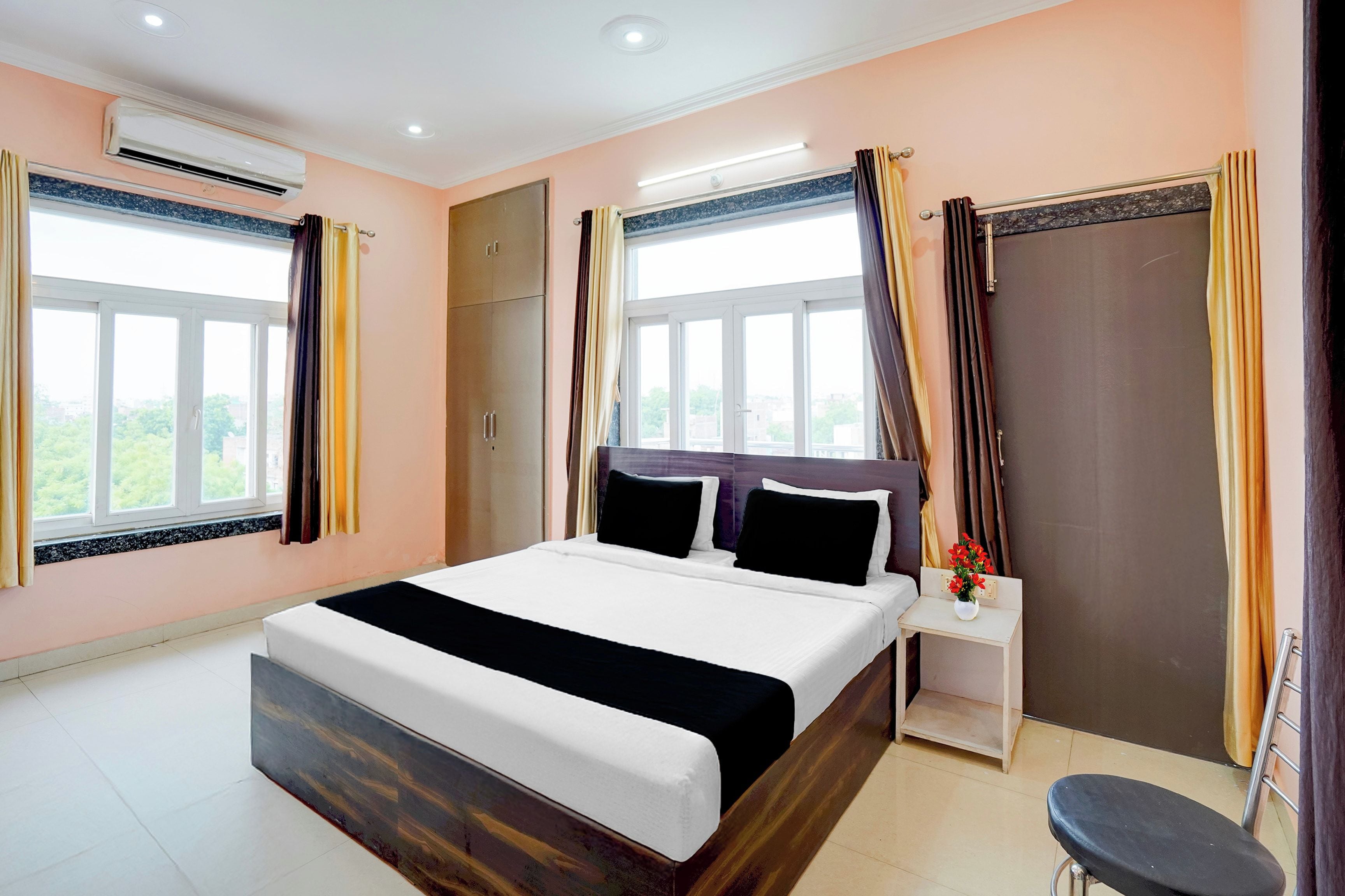 A hotel room with a bed, a nightstand, an air conditioning unit, and a view of the outdoors.