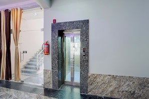 A hotel lobby with a marble floor, a fire extinguisher, a staircase, and a glass elevator. - Collection O IIT BHU Susu Wahi Varanasi (Varanasi)