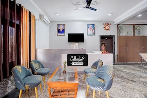 A modern living room with a glass coffee table, two blue chairs with gold leaf patterns, a flat-screen TV mounted on the wall, and a decorative clock. - Collection O IIT BHU Susu Wahi Varanasi (Varanasi)