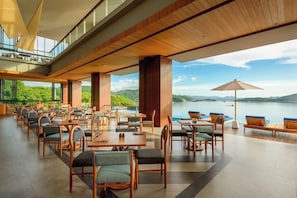 A spacious outdoor dining area with multiple tables and chairs, overlooking a body of water and hills. - Katamaran Hotel and Resort Komodo (Labuan Bajo)