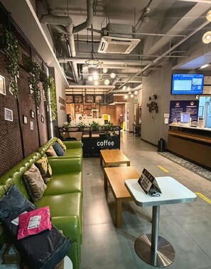 Un interior de cafetería moderna con un sofá verde, mesas de madera y una barra de café.