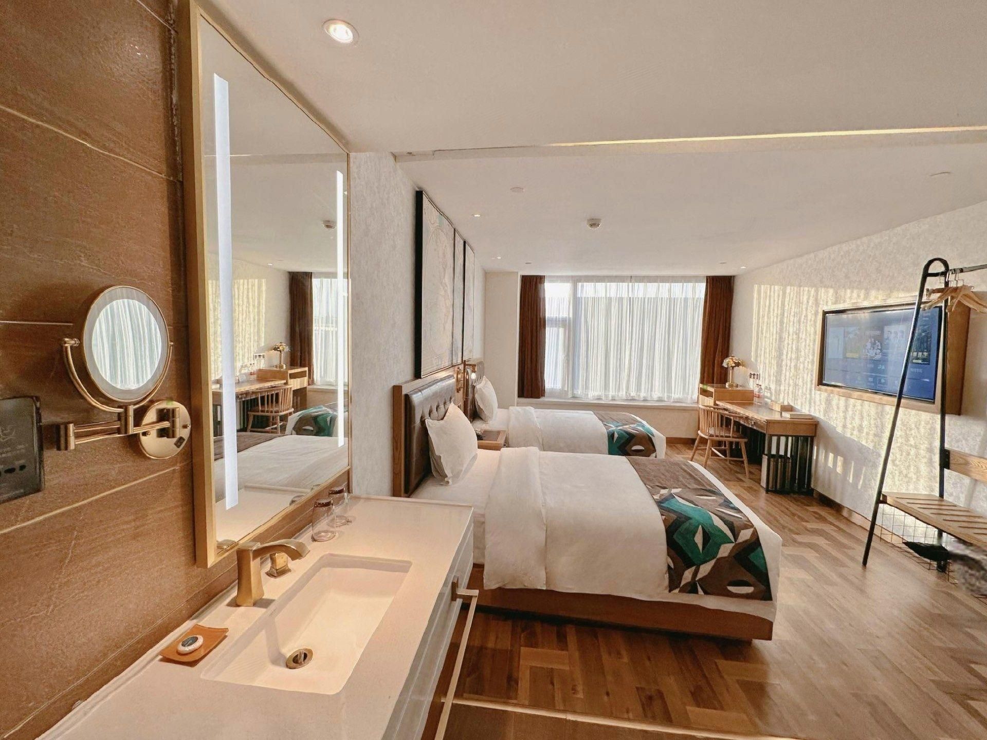 A hotel room with a large bed, a separate sitting area, a desk, a television, and a bathroom with a mirror and sink.
