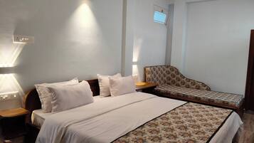 Habitación de hotel con cama, sofá, mesita de noche y lámpara de pared.