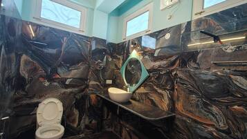 A bathroom with a marble wall, a white toilet, and a sink with a mirror.