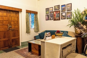 A cozy room with a wooden door, a small desk with a calendar, a sofa, and a wall adorned with framed pictures. - Tiggi's iing Heritage Homestay (Shillong)