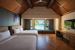 Habitación de hotel con dos camas, un escritorio, un televisor y vista al océano.