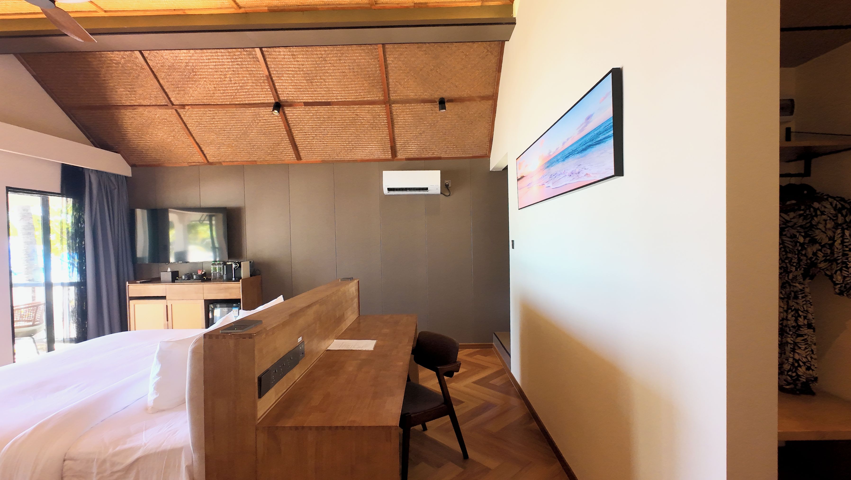 A hotel room with a bed, a desk, a chair, a TV, and an air conditioning unit.