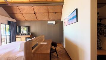 A hotel room with a bed, a desk, a chair, a TV, and an air conditioning unit.