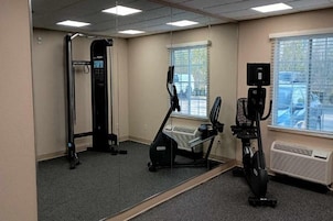 Un gimnasio con pared espejada, equipamiento de ejercicio y una ventana con persianas.