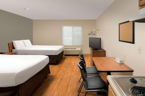 Habitación de hotel con dos camas, un escritorio, una silla, un televisor, un calentador y una ventana con persianas.