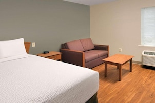Una habitación de hotel con una cama, una silla, una mesita y una ventana con persianas.
